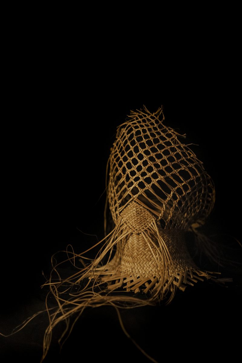 Raranga by Kade Cowper: an open-weave form trailing loose strands, lit against black.