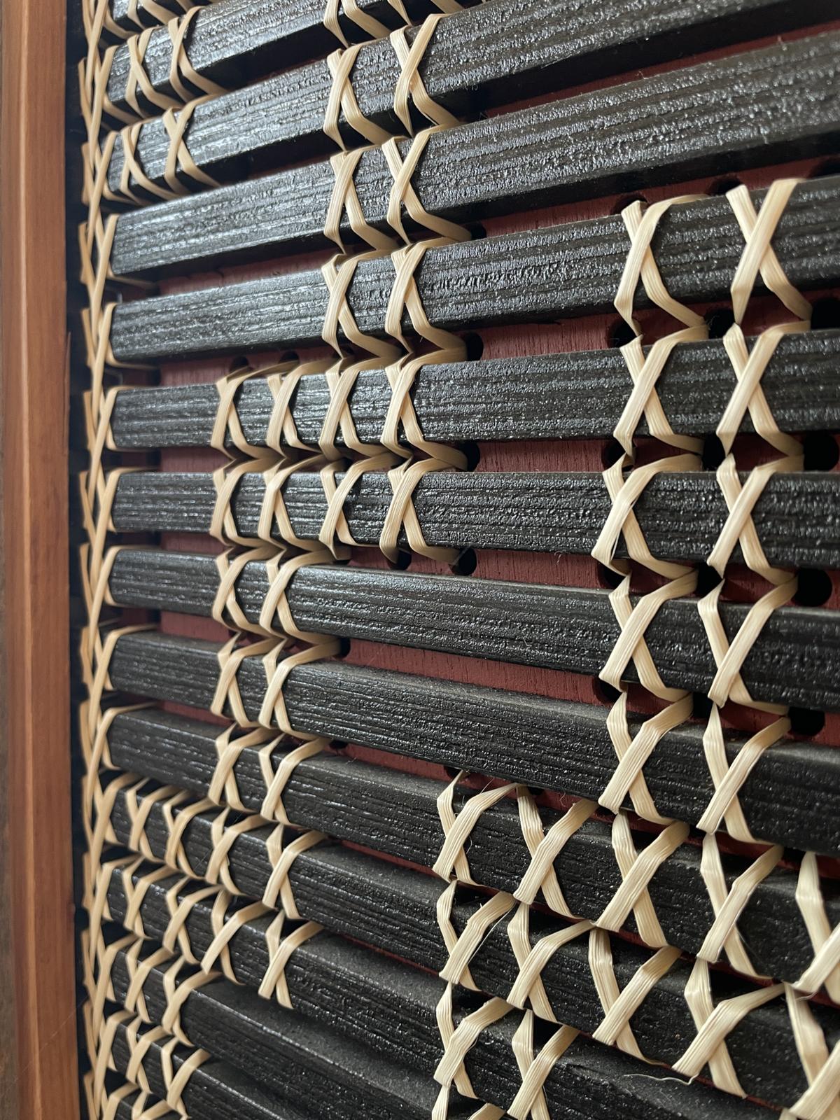 Poutama by Aka Whiro: the black slats and kiekie stitches seen at a low angle, the ochre red board showing between.