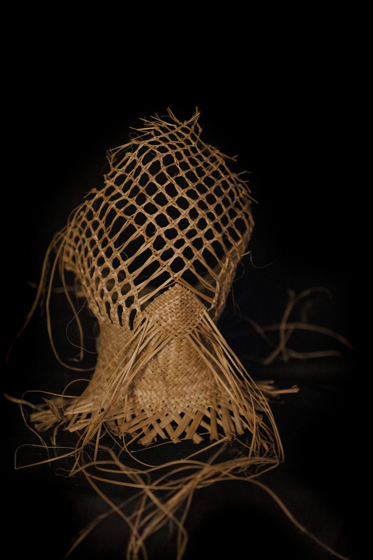 Raranga by Ruth Woodbury: an open-weave headpiece standing on its own, loose strands falling.
