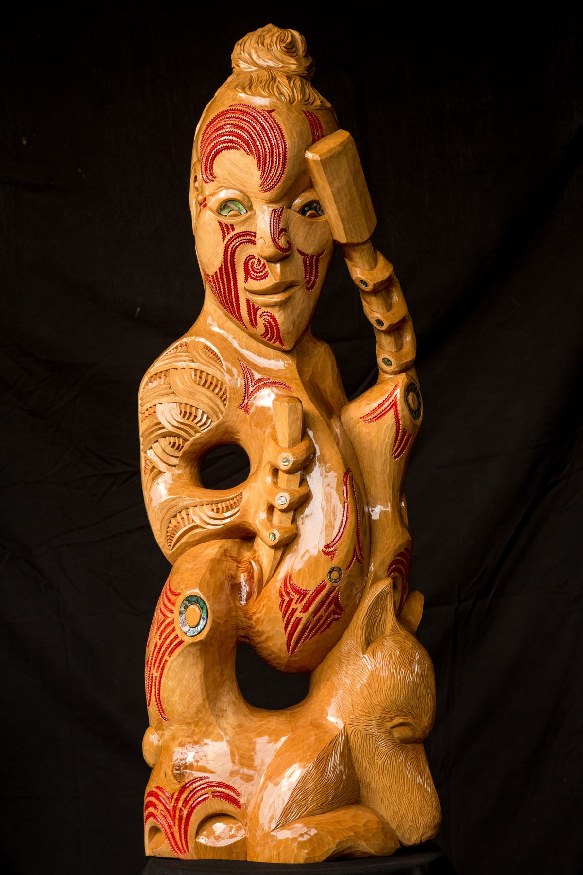Rua carving himself out of the log, red moko and a topknot, the mallet raised beside his head and the chisel at his body.