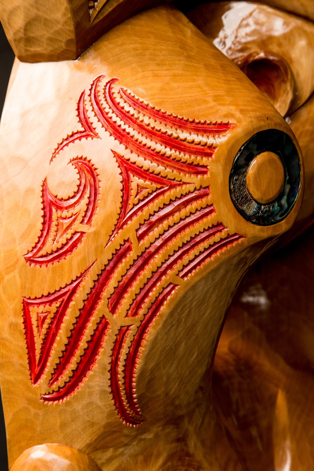 Rua: red moko lines and a pāua inlay, close.