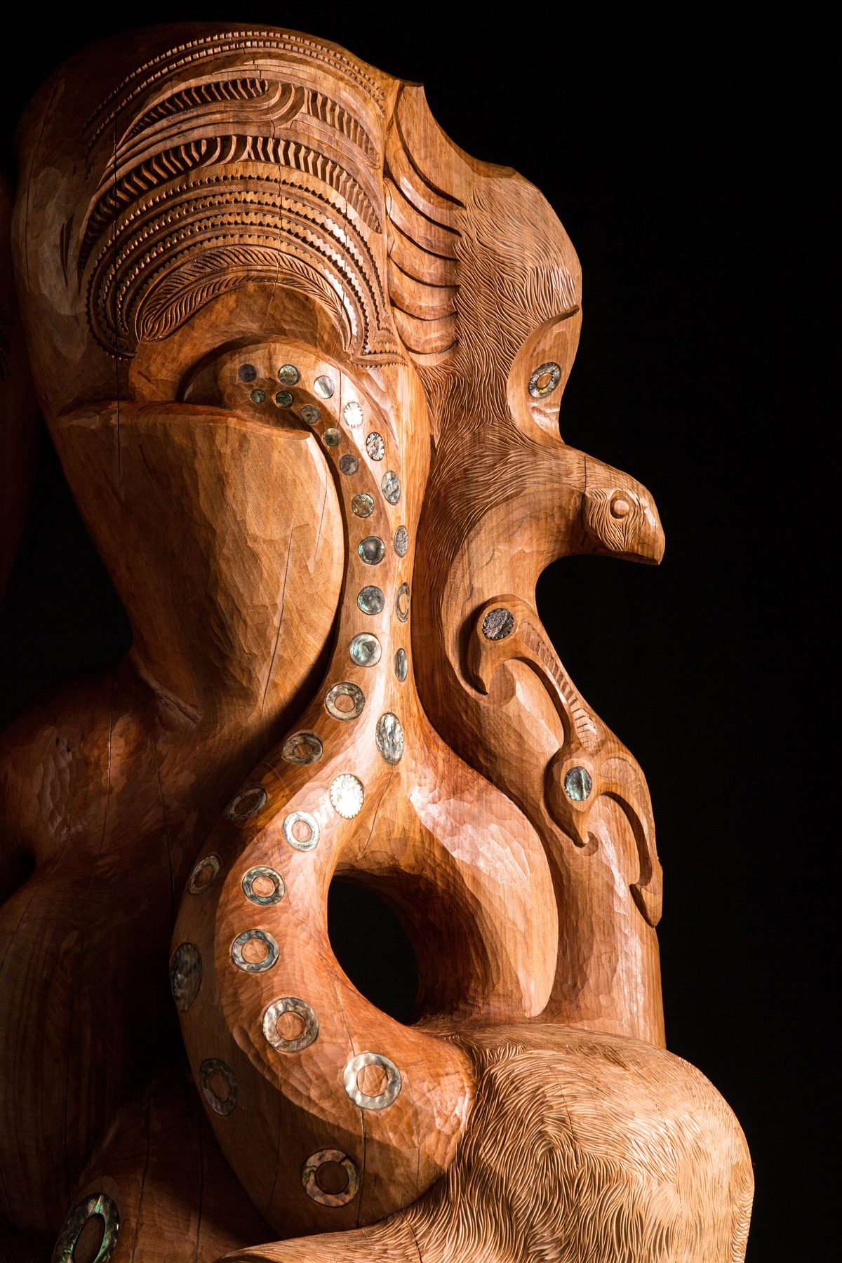 Te Ara Whakaiti: the tentacle inlaid with pāua enters below the rider's moko, the manu beside it.